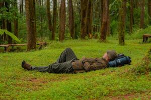 Asian adventurers enjoy the serenity of the wild by resting on the green grass in the pine forest area. A male adventurer was lying on the green grass in a quiet pine forest area. photo