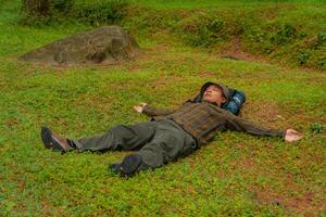 Asian adventurers enjoy the serenity of the wild by resting on the green grass in the pine forest area. A male adventurer was lying on the green grass in a quiet pine forest area. photo