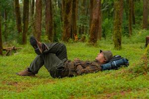 Asian adventurers enjoy the serenity of the wild by resting on the green grass in the pine forest area. A male adventurer was lying on the green grass in a quiet pine forest area. photo