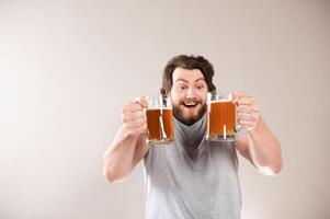 Cheerful young guy with glasses of foaming beer isolated on gray background, free space for advertising text photo