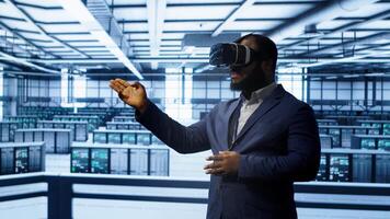 African american developer immersed in virtual reality at data center, doing units maintenance. Technician using VR headset to optimize servers performance, checking operations, camera A photo
