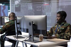 Government expert working in a high tech command post to gather intelligence from surveillance cctv systems. Soldier analyzing real time data and transmitting crucial field information for defense. photo