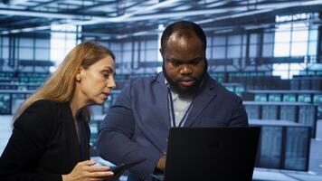 Teamworking technicians managing data center with advanced technology using devices. Coworkers in server room optimizing data center infrastructure with laptop and tablet, camera A photo