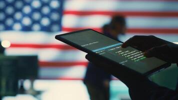 Cybersecurity expert in a governmental IT environment with the American flag. Monitoring cybersecurity, encryption and data security on a tablet to protect against cyber threats. Close up. Camera A. photo