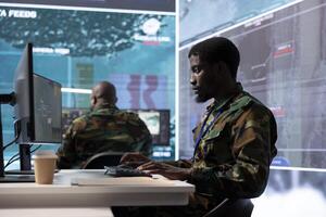 Army specialist in a command post uses high tech gear and big screen to gather crucial information, supporting field operations. Studying classified documents to support strategic planning. photo