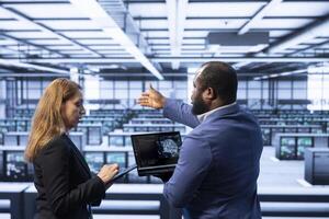 Team of technicians in data center using laptop to visualize artificial intelligence neural networks made up of interconnected nodes. Teamworking colleagues oversee AI systems processing information photo