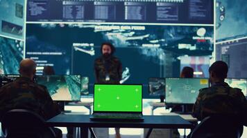 Laptop showing isolated mockup screen in army base of operations, military personnel working on gathering crucial information for a new mission. General headquarters with high tech. Camera B. photo