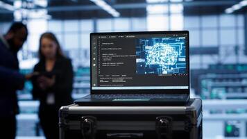Focus on laptop in data center with artificial intelligence brain used by engineers in blurry background. Close up of device displaying AI deep learning software in server farm, camera A photo