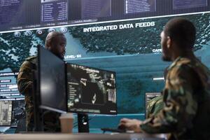 Cybersecurity team operates in an advanced military command center, managing surveillance systems and data protection. Army personnel work on national security operations using high tech gear. photo