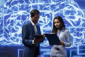 IT department coworkers solving tasks on laptop and tablet, running artificial intelligence programming scripts. Team of technicians brainstorming ways to develop AI applications photo