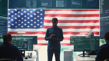 Cybersecurity expert working in a governmental hacking room with the American flag shown on big screen. Safeguarding data protection and doing cyber threat analysis in a high tech office. Camera B. photo