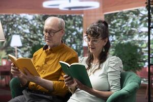Senior people reading a literature book relaxing together at home, sitting on the couch and enjoying lecture. Feeling good with free time for leisure during retirement, companionship. photo