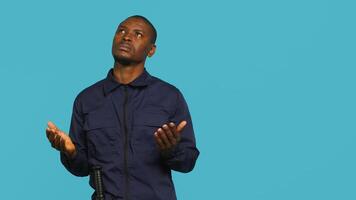 Portrait of security guard waiting for miracle, putting hands together while overseeing premises. Private law enforcement worker looking to sky, praying, studio backdrop, camera A photo