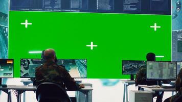 Diverse group of privates operating on a big screen isolated display, looks at a greenscreen and gathering intelligence to help with military operations in command center. Army facility base. Camera A. photo