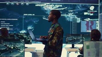 Army officer examines satellite radar footage to gather intelligence for a new mission, operating in military headquarters power base with his crew. Federal agency officers in control room. Camera B. photo