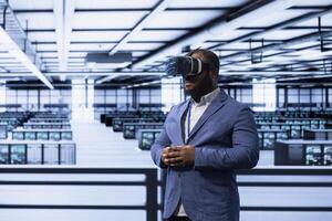 Admin working in data center, using VR headset to configure network infrastructure. IT specialist in server hub looking for technical issues using virtual reality technology photo