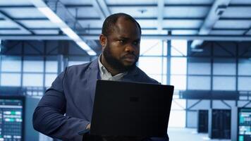 Computer scientist in data center using diagnostic tools and system monitoring software on laptop to identify cause of errors. IT specialist in server farm establishment repairing equipment, camera A photo