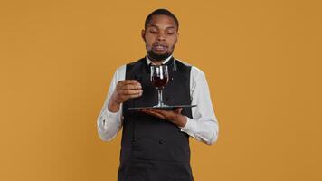 Waiter serving clients with a glass of red wine before dinner, recommending a special drink for customer satisfaction. Employee carrying a tray and serves people with professionalism. Camera B. photo