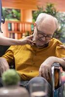 Nurse jumping to help senior man in wheelchair losing conscience during home visit, old person hyperventilating and scaring his wife. Medical assistant in panic checking the pulse. Close up. photo