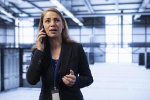 Businesswoman speaking on phone in high tech data center housing advanced computing equipment. IT expert delegating tasks in technologically advanced environment during telephone call photo