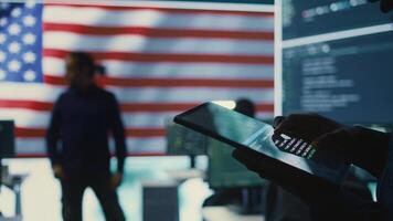 Cybersecurity expert in a governmental IT environment with the American flag. Monitoring cybersecurity, encryption and data security on a tablet to protect against cyber threats. Close up. Camera B. photo
