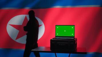 North Korea secret police agent uses mass propaganda tools on green screen laptop to influence population minds. Pyongyang regime commits PsyOp sabotage using mockup device, camera B photo