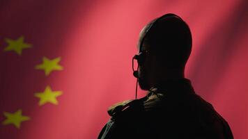 Military dispatcher working for Chinese Communist Party providing informations for troops using headset. Radio communications operator isolated over China flag background coordinating troops, camera B photo