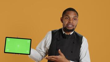 Catering employee presenting an isolated chroma key display while he wears an apron and serving clients at diner. Hospitality industry staff in professional attire, customer satisfaction. Camera A. photo