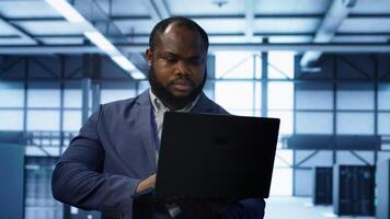 Computer scientist in data center using diagnostic tools and system monitoring software on laptop to identify cause of errors. IT specialist in server farm establishment repairing equipment, camera A photo