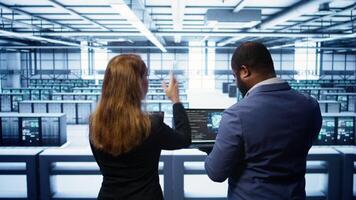 Teamworking programmers in data center overseeing server operations using laptop and tablet. Coworkers ensuring optimal performance and data integrity in server room using devices, camera B photo