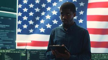 Cybersecurity expert working in a governmental hacking room with the American flag shown on big screen. Safeguarding data protection and doing cyber threat analysis in a high tech office. Camera A. photo