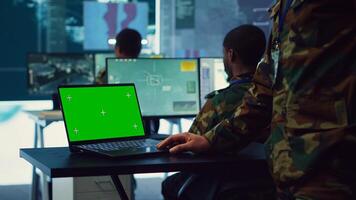 Army officer studies isolated greenscreen display on a laptop in control room, military power base personnel monitoring satellite world map for federal operations. Commander in uniform. Camera A. photo