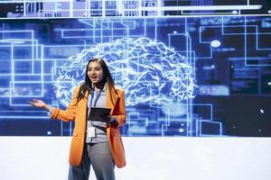 Upbeat programmer using tablet during presentation, exploring ways emerging AI technologies can enhance businesses. Jolly woman at event presents artificial intelligence using device and microphone photo