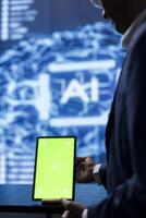Technician in startup doing advancements in AI field using chroma key tablet. Close up of green screen device used by IT expert working in cutting edge workspace featuring artificial intelligence photo