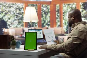 Business owner manages financial plans next to a mockup display on tablet, using annual sales analytics and reports to increase the profit. Entrepreneur does budget analysis at home. photo