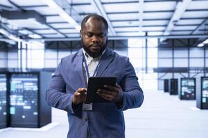 Programmer walking in data center, monitoring system performance with tablet, identifying bottlenecks and implementing optimizations to improve efficiency. Server hub IT expert troubleshooting malfunctions photo