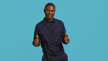 Portrait of joyous security guard doing thumbs up sign gesturing with finger while overseeing premises. Private law enforcement worker doing positive hand gesture, studio backdrop, camera B photo