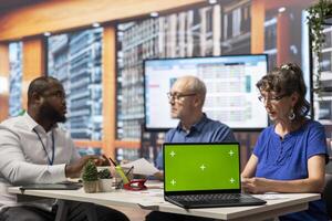 Senior clients discussing with financial planner to develop a secure pension plan, having a laptop with chroma key display. Explore retirement options to cover savings and insurance. photo