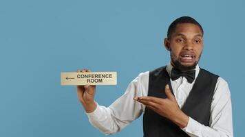 Hotel concierge using a wall indicator to guide clients to the conference room, presenting various amenities at the five star luxury resort. Bellboy staff holds a sign for directions. Camera A. photo