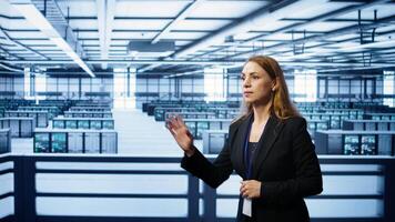 Software developer looking at holograms in data center, monitoring infrastructure. Woman in server room interacting with high tech augmented reality AI visualization, camera B photo
