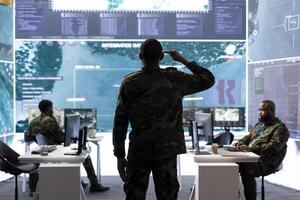 Special operations agent saluting his military crew in control center, showing respect with the honorary salute. Soldier working with staff on intelligence gathering for national security. photo