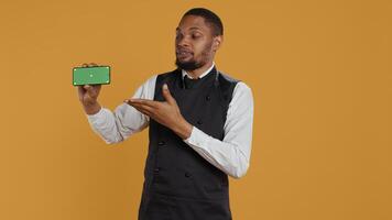 Waiter with professionalism holding a phone with isolated mockup display, working in dining and eatery industry. Friendly restaurant staff does customer oriented activity at his job. Camera B. photo