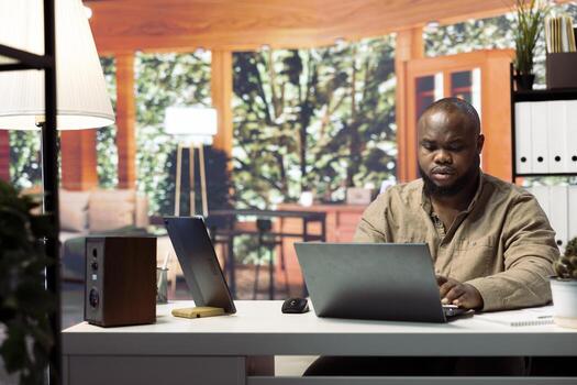 Entrepreneur sitting at his desk working on a laptop with wireless technology for remote job efficiency. Analyzing data and developing strategies, successful telecommuting from home office. photo