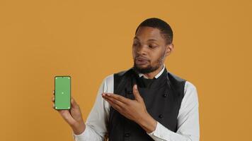 Restaurant staff showing a smartphone with green screen in studio, prepared to serve food orders in service oriented environment. Waiter with apron and uniform serving clients at tables. Camera A. photo