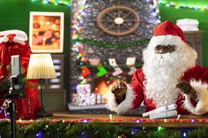 Father Christmas preparing to read letters on live stream online from his cozy workshop. Black Santa Claus recording a broadcast to spread festive magic for children all over the world. photo