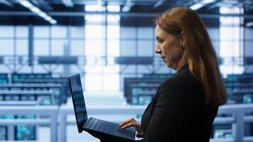 System administrator in server hub checking recovery plan on laptop, monitoring energy consumption. IT expert uses notebook in data center workspace, ensuring rigs are functioning optimally, camera A photo