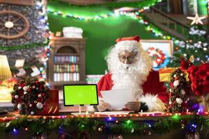 Santa Claus checking his naughty or nice list next to isolated mockup, preparing for his journey around the world to bring gifts on Christmas eve. Old man making children happy on x mas. photo
