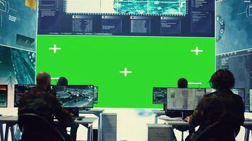 Diverse group of privates operating on a big screen isolated display, looks at a greenscreen and gathering intelligence to help with military operations in command center. Army facility base. Camera B. photo