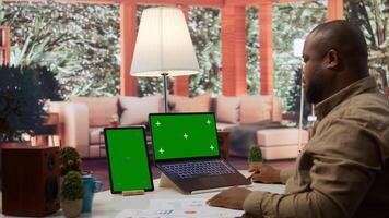 Business owner works from his home with isolated mockup screen and annual data reports for the financial situation. Entrepreneur examines profit numbers for performance metrics. Camera B. photo