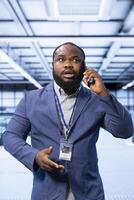Management executive overseeing operations in cutting edge data center, coordinating tasks during telephone call. IT expert in server hub managing systems and communicating via smartphone photo